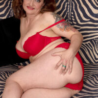 Middle-aged ginger-haired Amelie Azzure bares her humungous tits and smoothly-shaven gash from a crimson dress